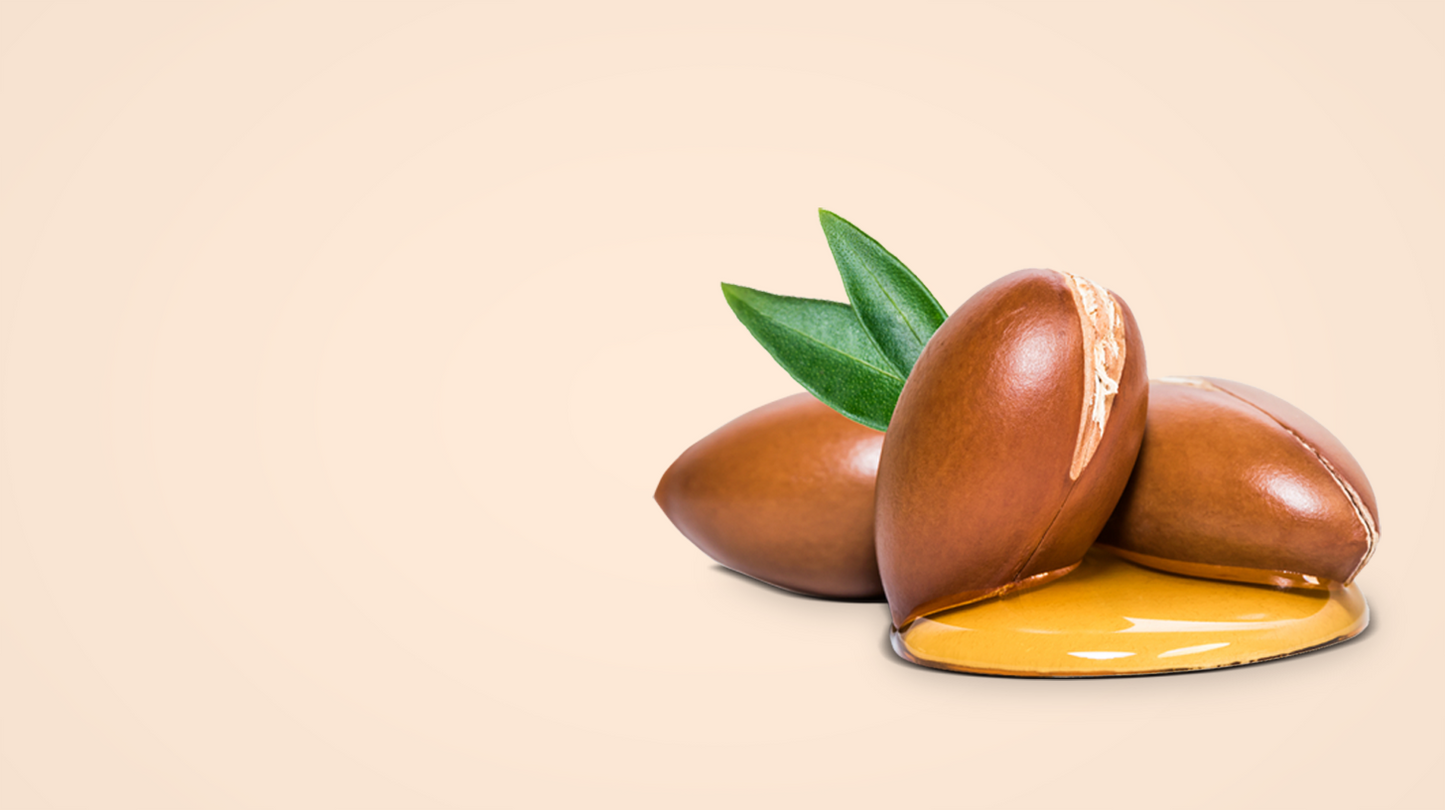 Three brown argan nuts with a green leaf on a beige background